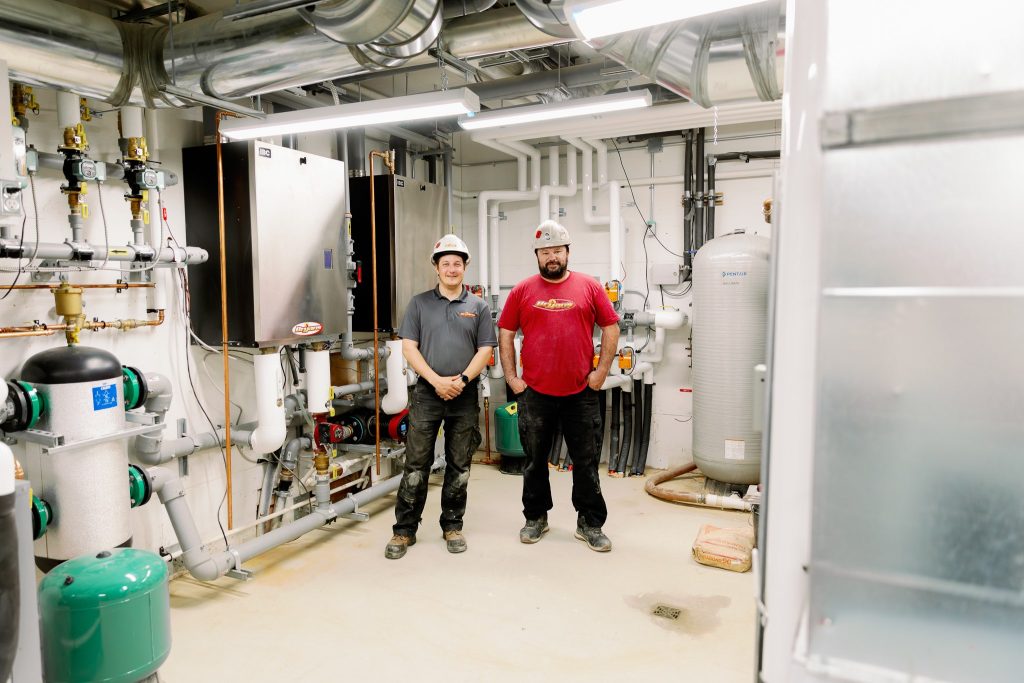 two people wearing hardhats standing in a bright clean hvac maintenance room