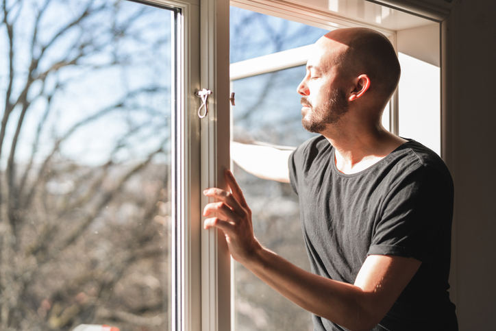 A man opening a window to breathe in fresh air.