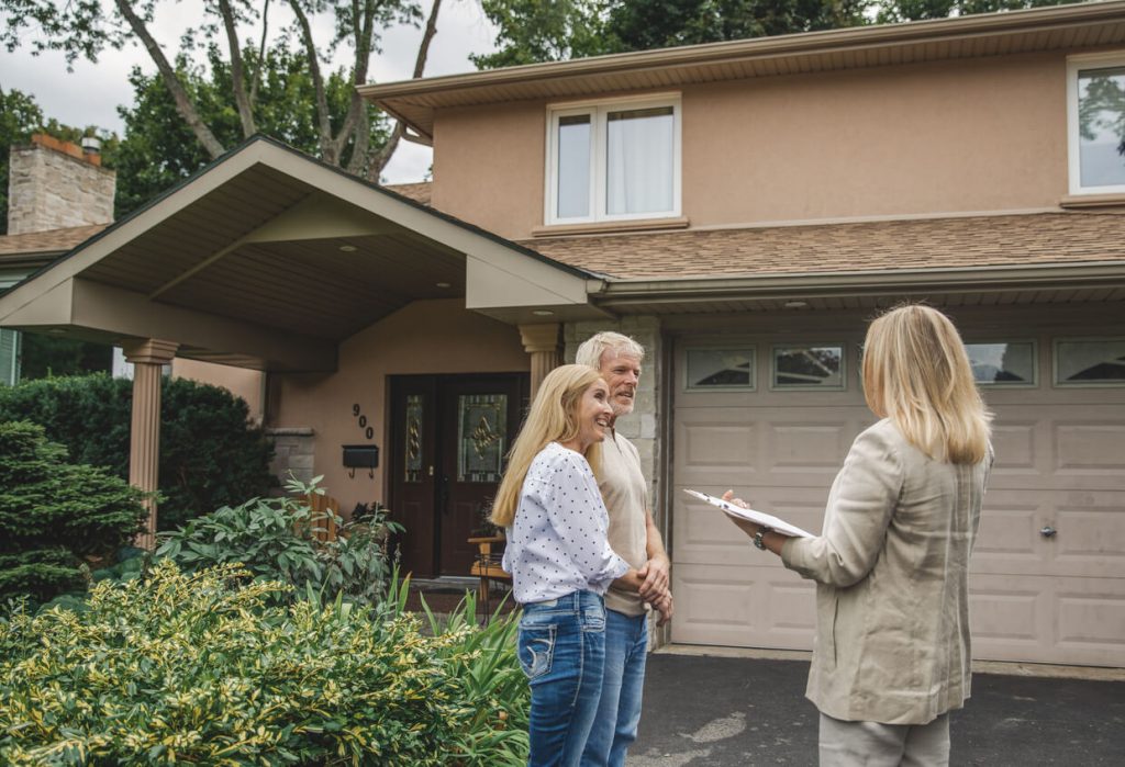 A photo of a couple standing with a home inspector outside of their two story house in the fall.
