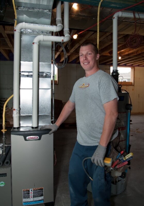 A photo of a Bryan's Fuel technician standing beside a furnace in the basement of a home. 