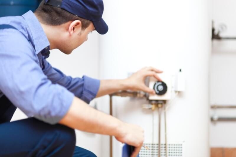 A photo of an HVAC technician adjusting the settings of a water heater.