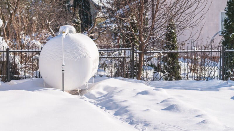 A photo of a residential propane tank in a yard in winter, covered in snow. 