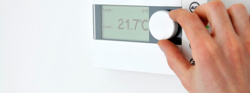 A photo of a hand adjusting the temperature on an oil furnace thermostat.