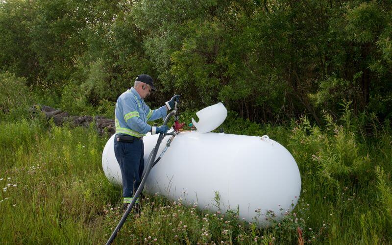 A Bryan's Fuel team member filling a propane tank located in a grassy field by trees.