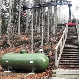 A photo of Bryan's Fuel installing a propane tank at the bottom of a wooded hill, with a crane.