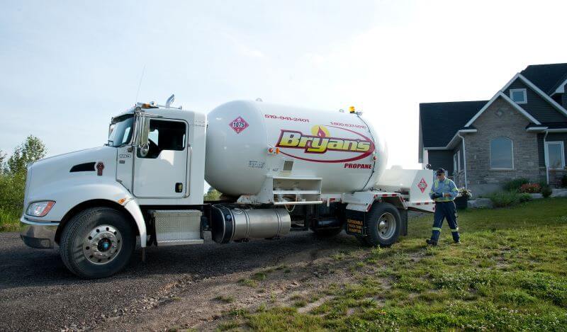 A photo of a Bryan's Fuel propane truck in the driveway of a rural home in the summer.