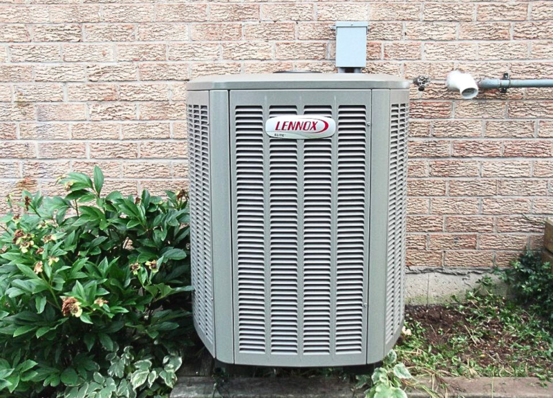 A photo of an Lennox air conditioner unit installed at the side of a house in summer.