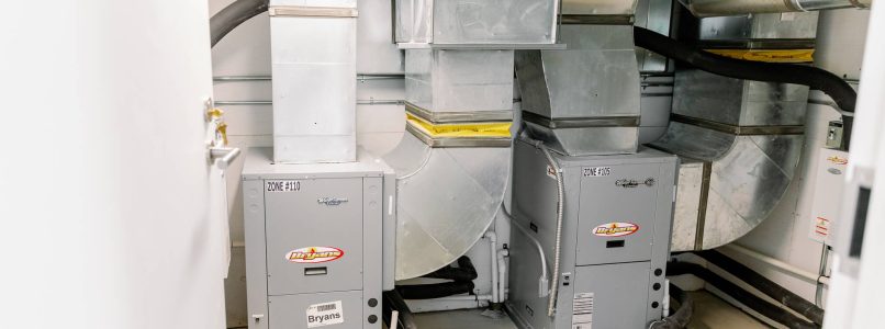 The image shows an indoor HVAC system with two large metal furnaces and extensive ductwork installed in a utility space.
