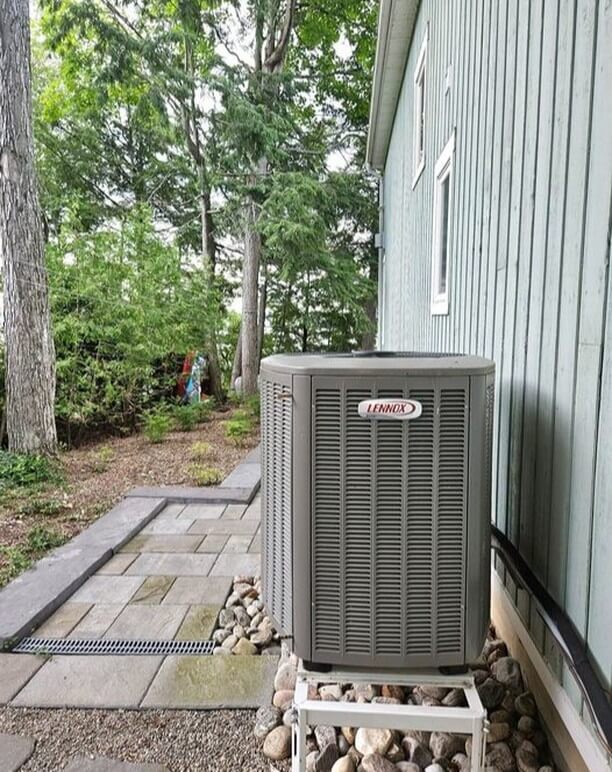 A photo of a heat pump installed at the side of a rural house in summer by Bryan's Fuel.
