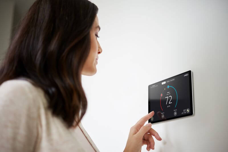 A photo of a woman adjusting a smart thermostat on the wall of her home.