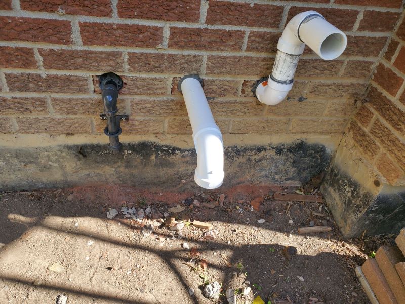 A photo of white PVC pipes on the side of a brick house.