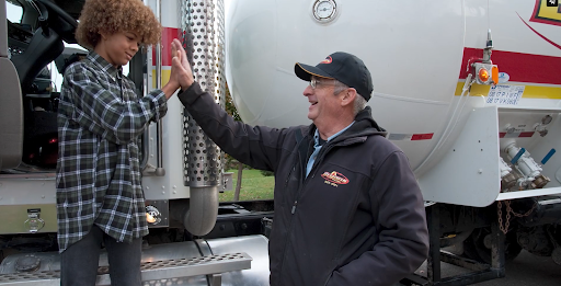 A Bryan's Fuel team member giving a high-five to a child standing on the step of a propane truck.