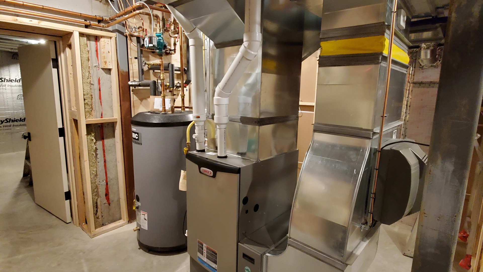 A basement with a furnace, water heater, and air duct system. Exposed wooden framework and pipes are visible, suggesting ongoing construction.