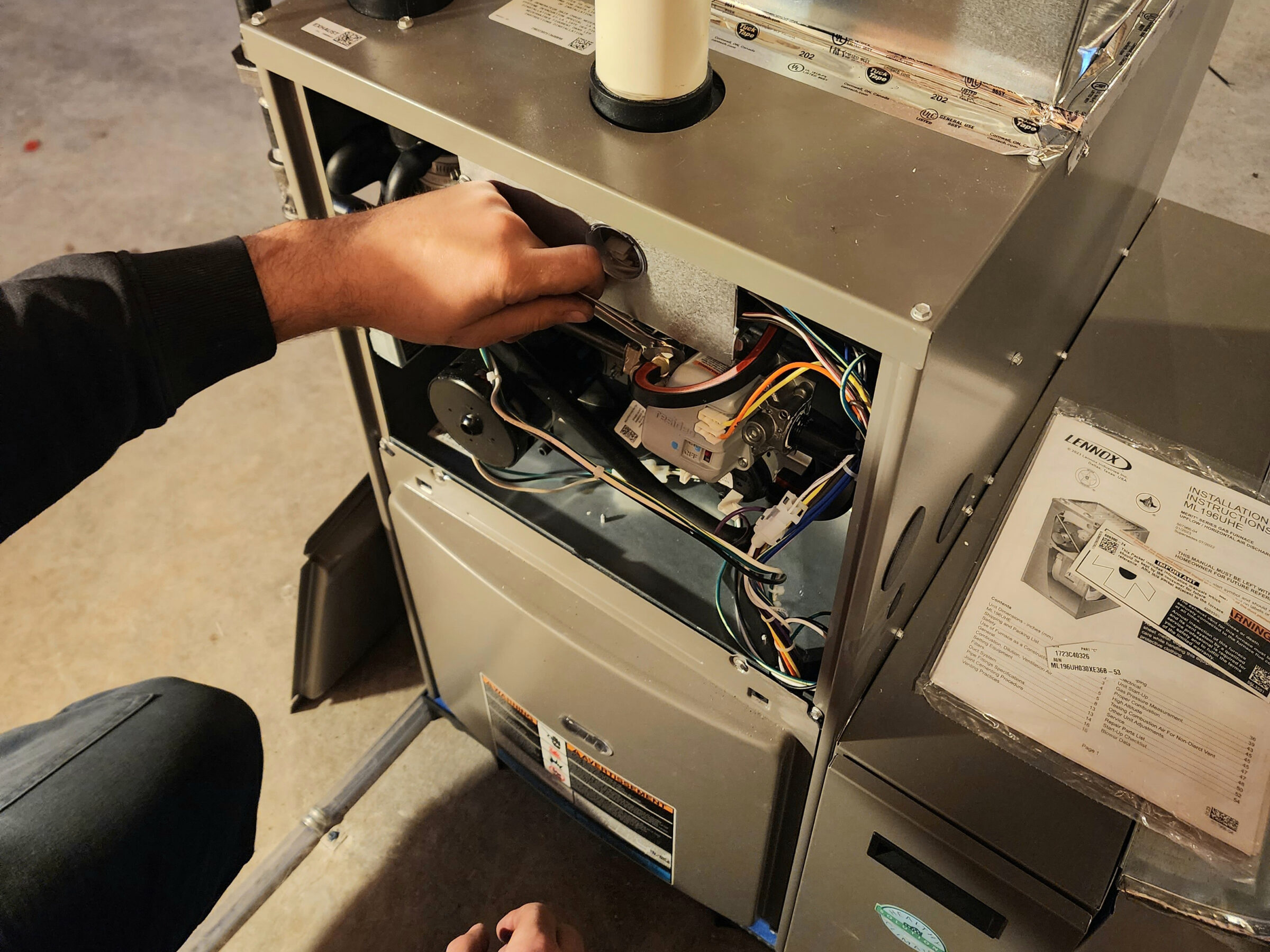 A person installs or repairs a Lennox HVAC unit, with wires and instructions visible in a workshop setting.