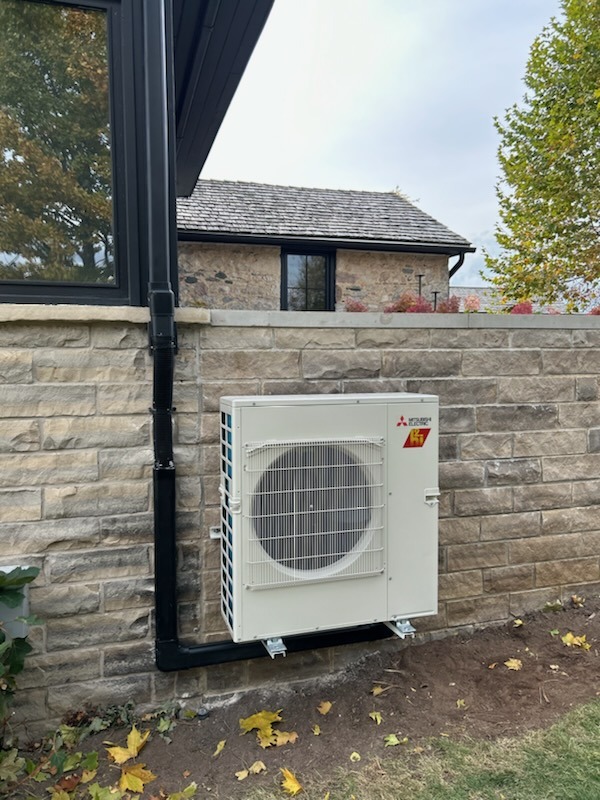 A stone building with a Mitsubishi air conditioning unit mounted outside, near a window, surrounded by autumn leaves and trees.
