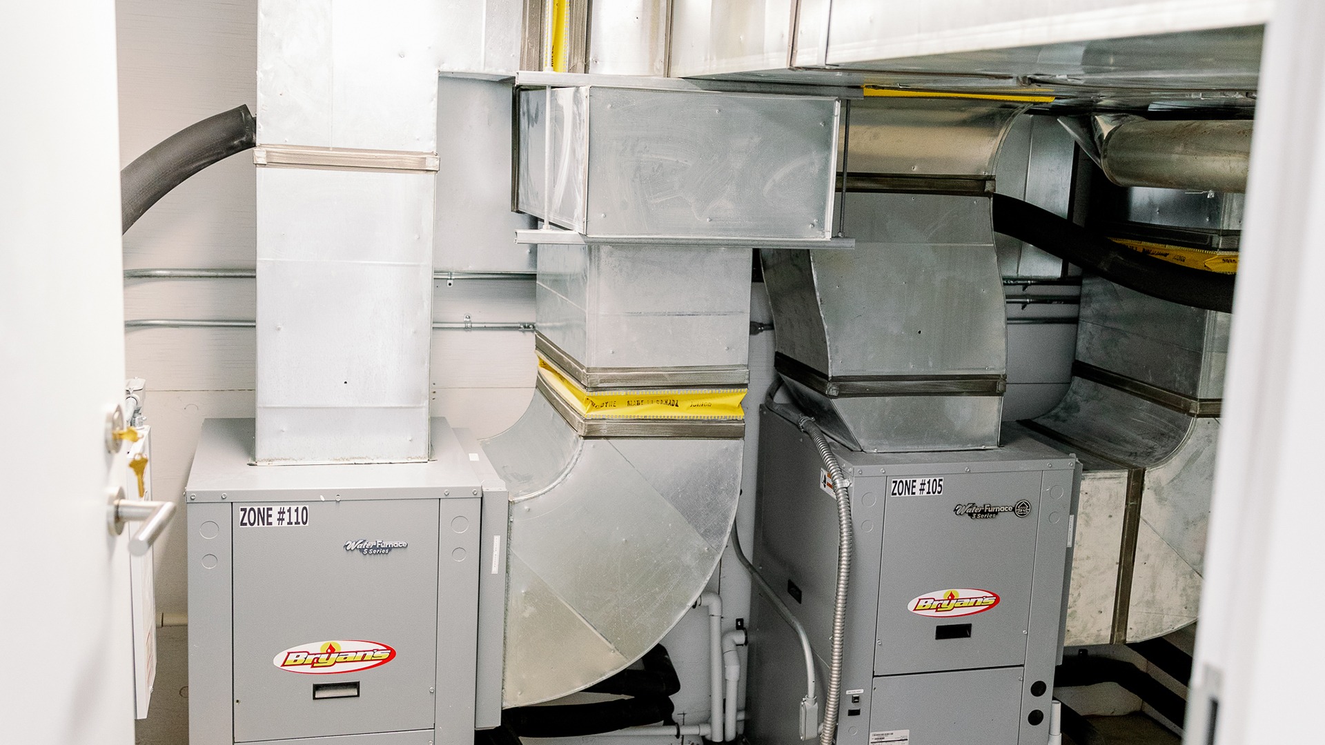 Industrial HVAC system with metallic ducts and furnaces labeled "Zone #110" and "Zone #105," capturing functional, modern indoor climate control equipment.
