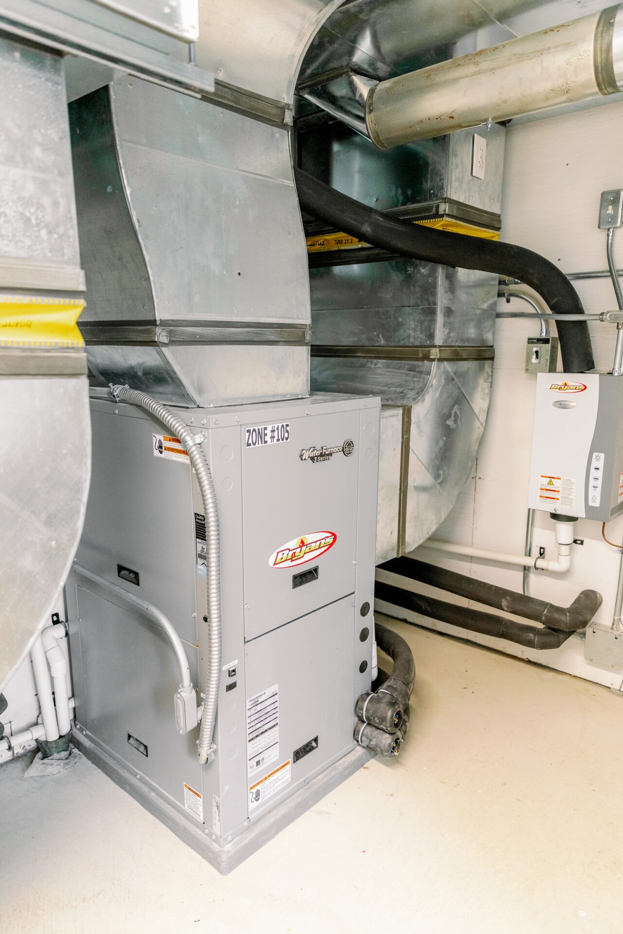 A Bryant HVAC system with ductwork is installed in an indoor area, featuring metallic pipes and insulation tubing for climate control.