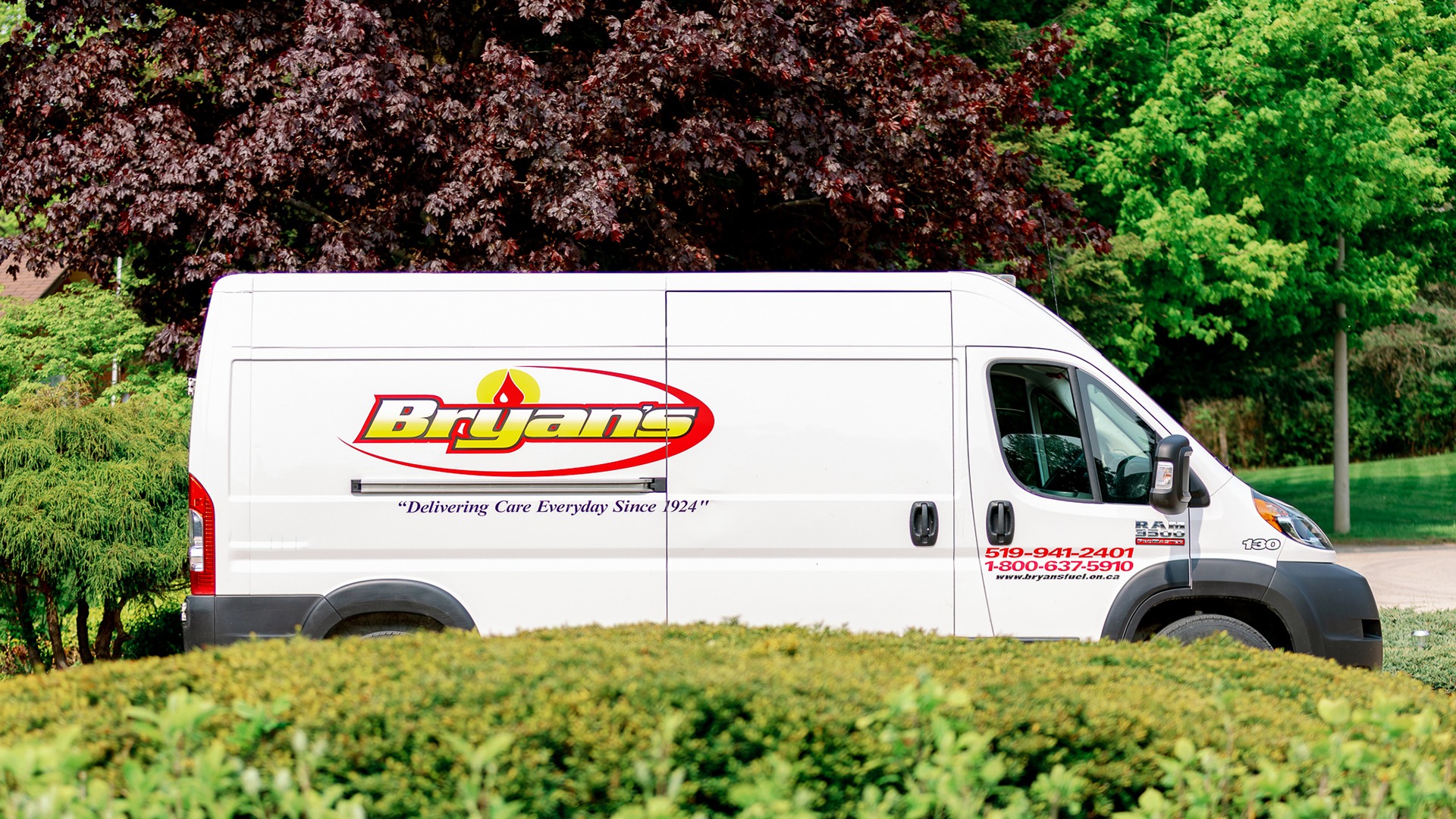 A white delivery van with "Bryan's" logo is parked near a lush green garden and trees. No recognizable landmarks are visible.