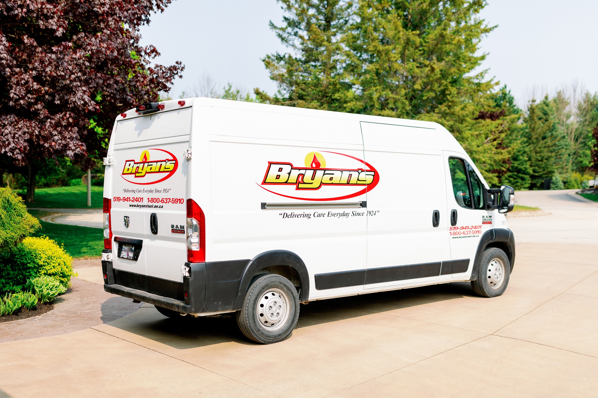 White van branded "Bryan's," parked in a driveway surrounded by green trees. Contact information and slogan visible on vehicle. Sunny day.
