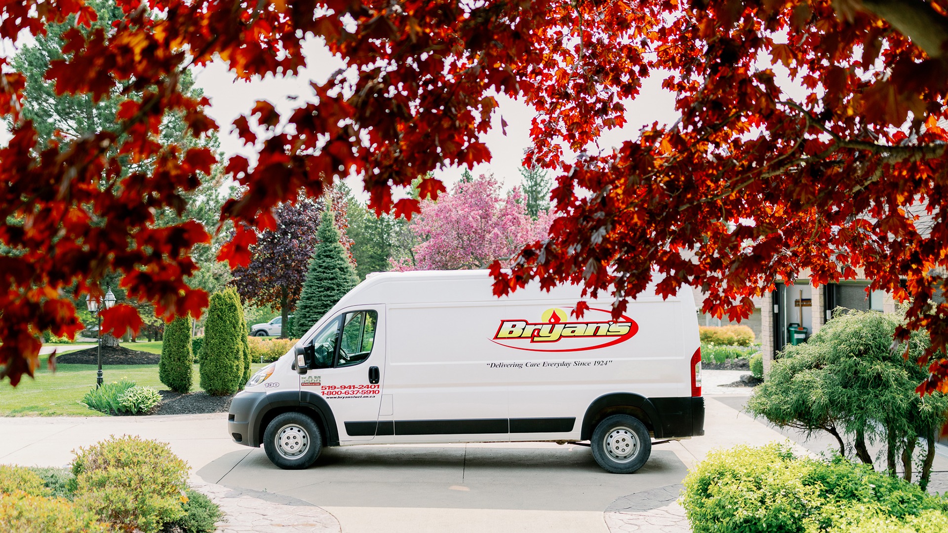 A white van labeled "Bryan's" is parked in a driveway surrounded by vibrant trees and neatly landscaped greenery.