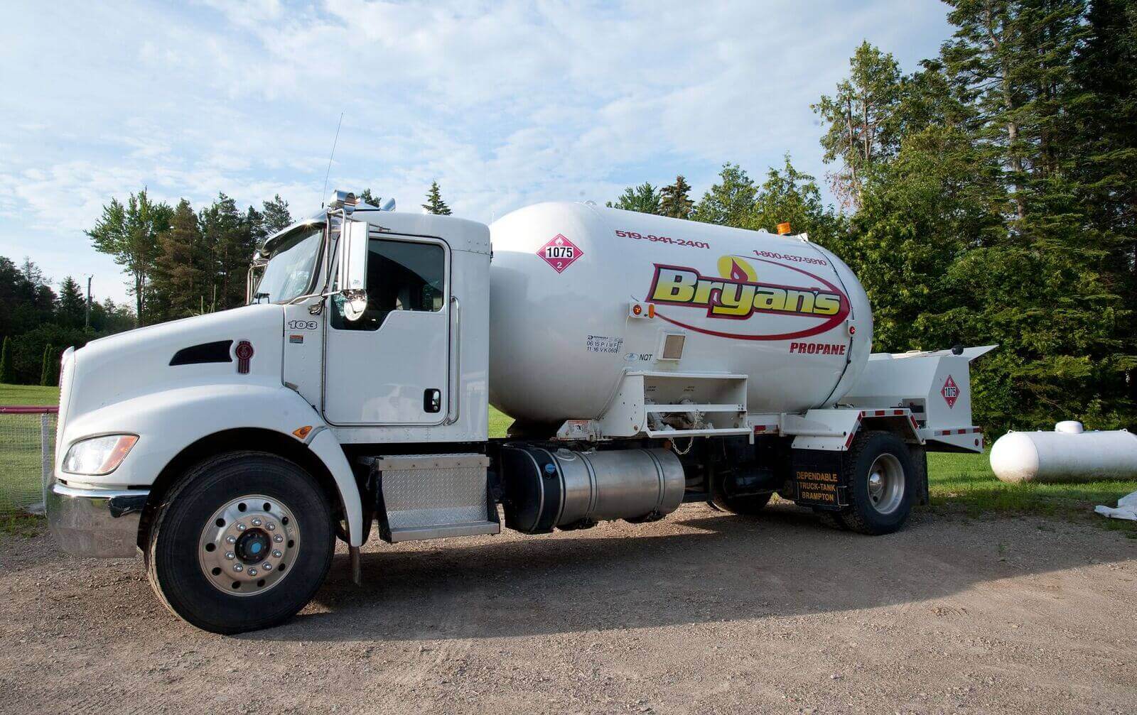 A white propane delivery truck labeled "Bryans" is parked on a gravel path, surrounded by trees under a partly cloudy sky.