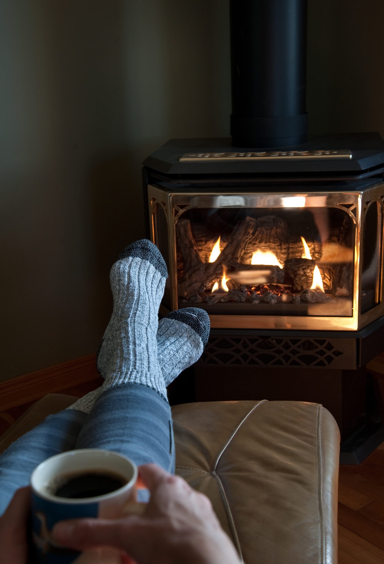 A person with cozy socks relaxes, sipping coffee by a warm, lit fireplace, creating a peaceful and inviting atmosphere indoors.