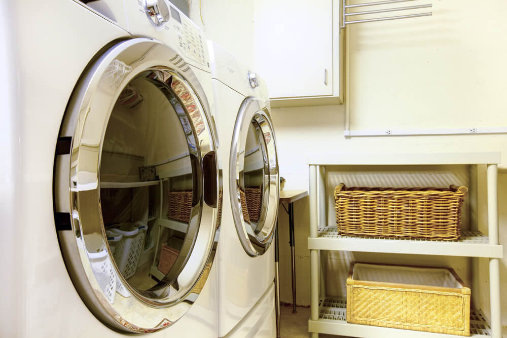 Modern laundry room featuring two front-loading washing machines and wicker baskets on shelves. The space is organized and brightly lit.