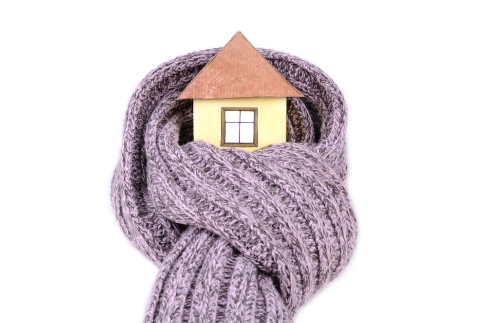 A small house model wrapped in a thick, knitted gray scarf, symbolizing warmth and coziness for a home.