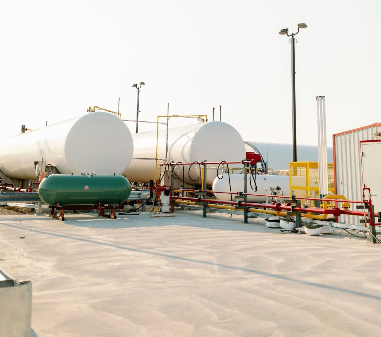 Industrial site with large propane tanks, pipelines, and equipment on a concrete surface. No people or recognizable landmarks are visible.