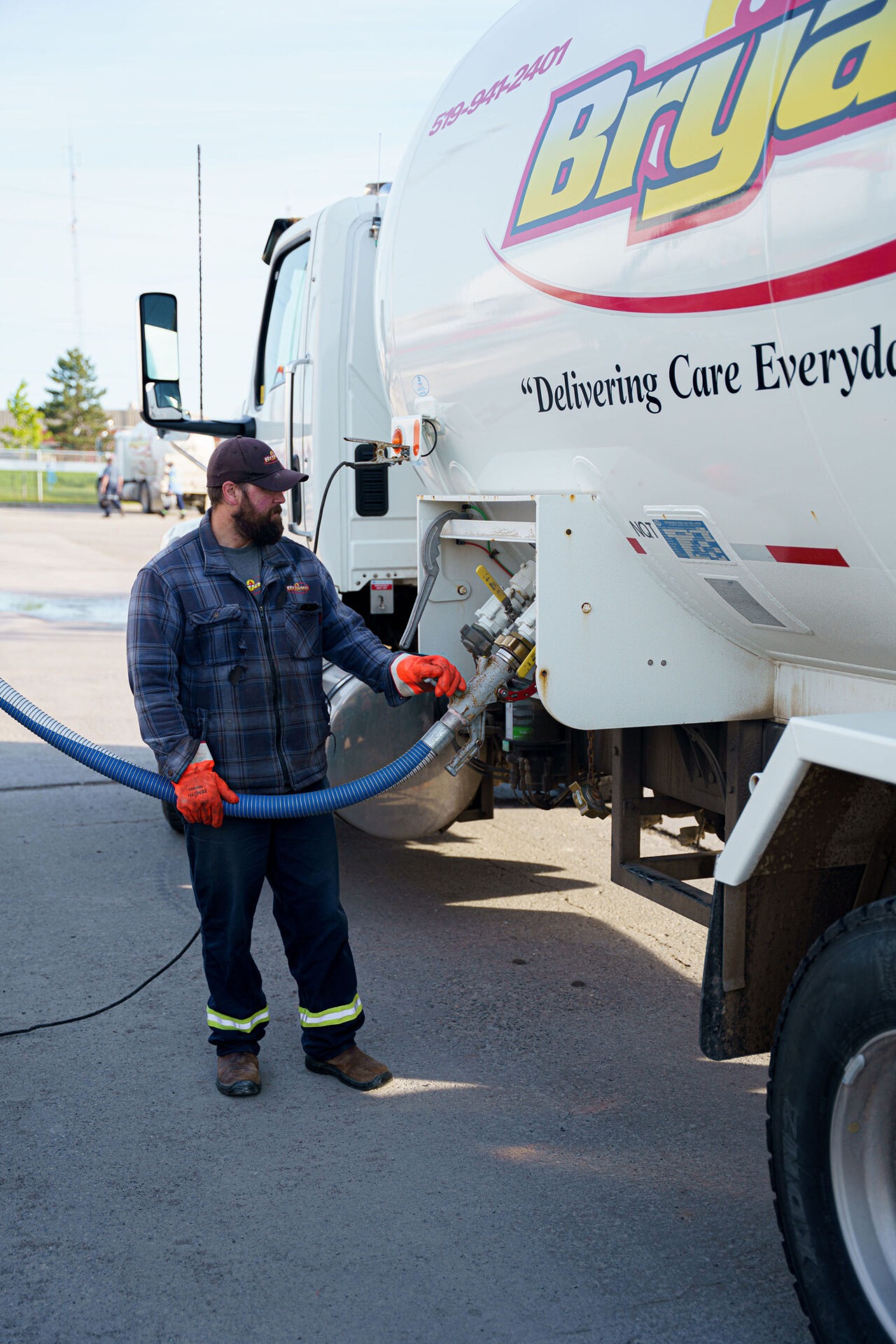A person in gloves operates a hose connected to a large truck labeled "Delivering Care Everyday" in an industrial setting.