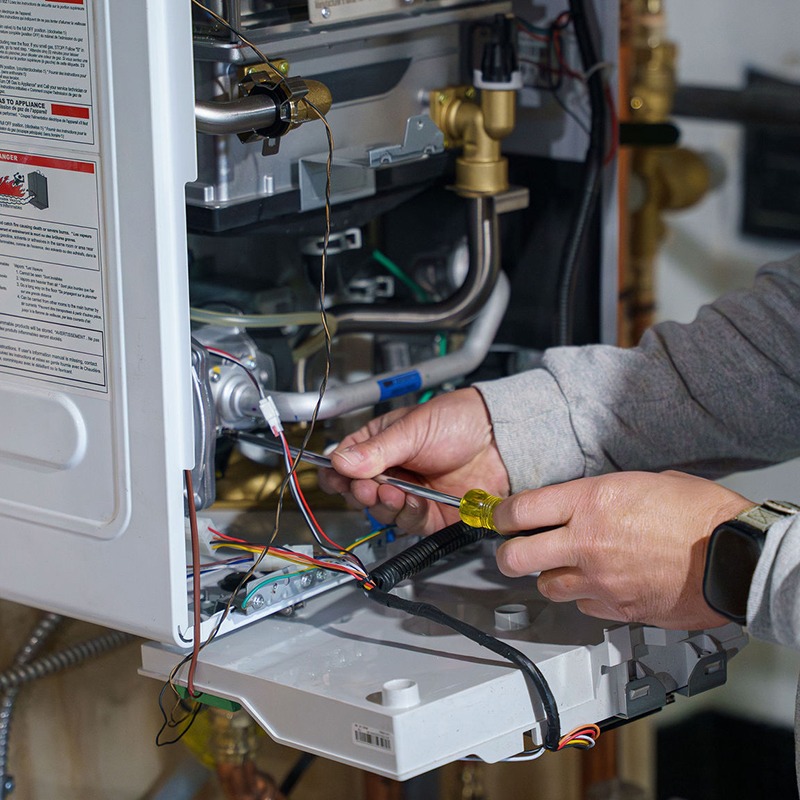 A person is repairing an electrical appliance, using a screwdriver, surrounded by wires and components in a mechanical setting.