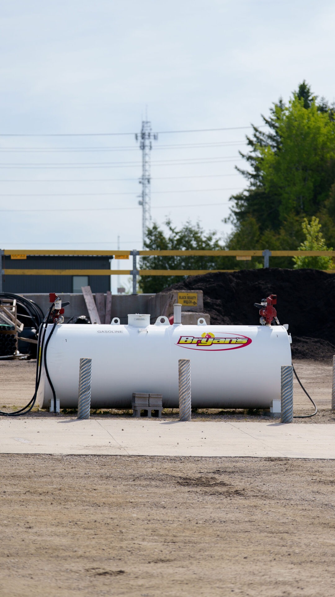 A large gas tank labeled "Bryan's" is situated in an outdoor area with surrounding machinery and trees. No recognizable landmarks or historical buildings.