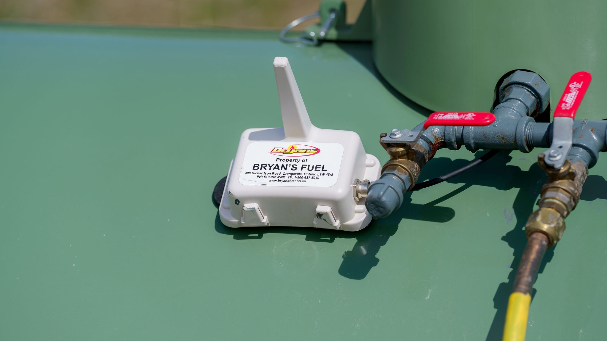 White device on a green surface with pipes and red valves. Label reads "Bryan's Fuel" with contact information and website.