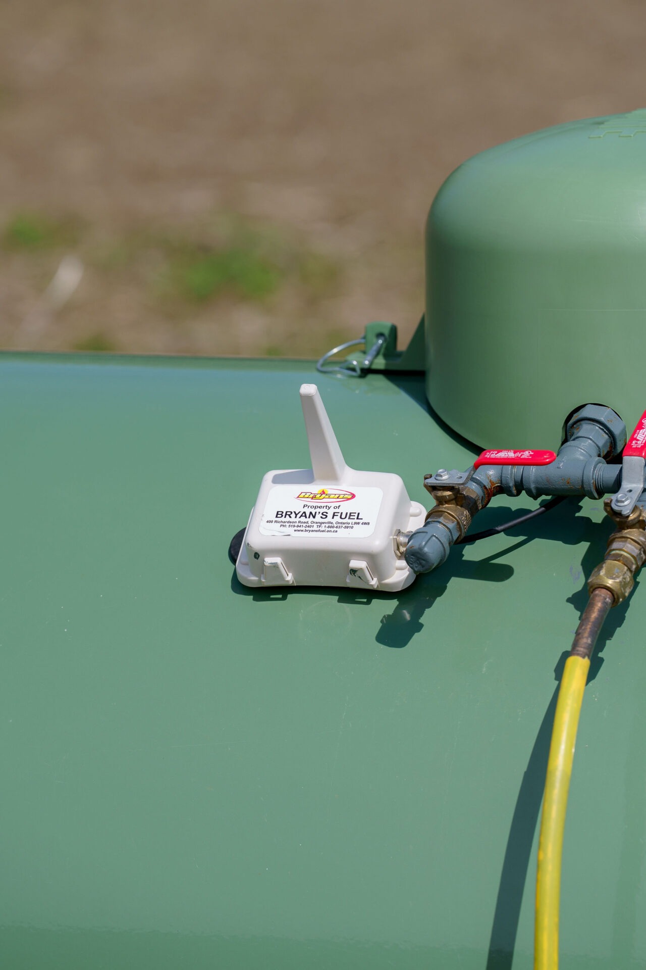 A green fuel tank with valves and a white device labeled 'Bryan's Fuel' is shown against a blurred background.