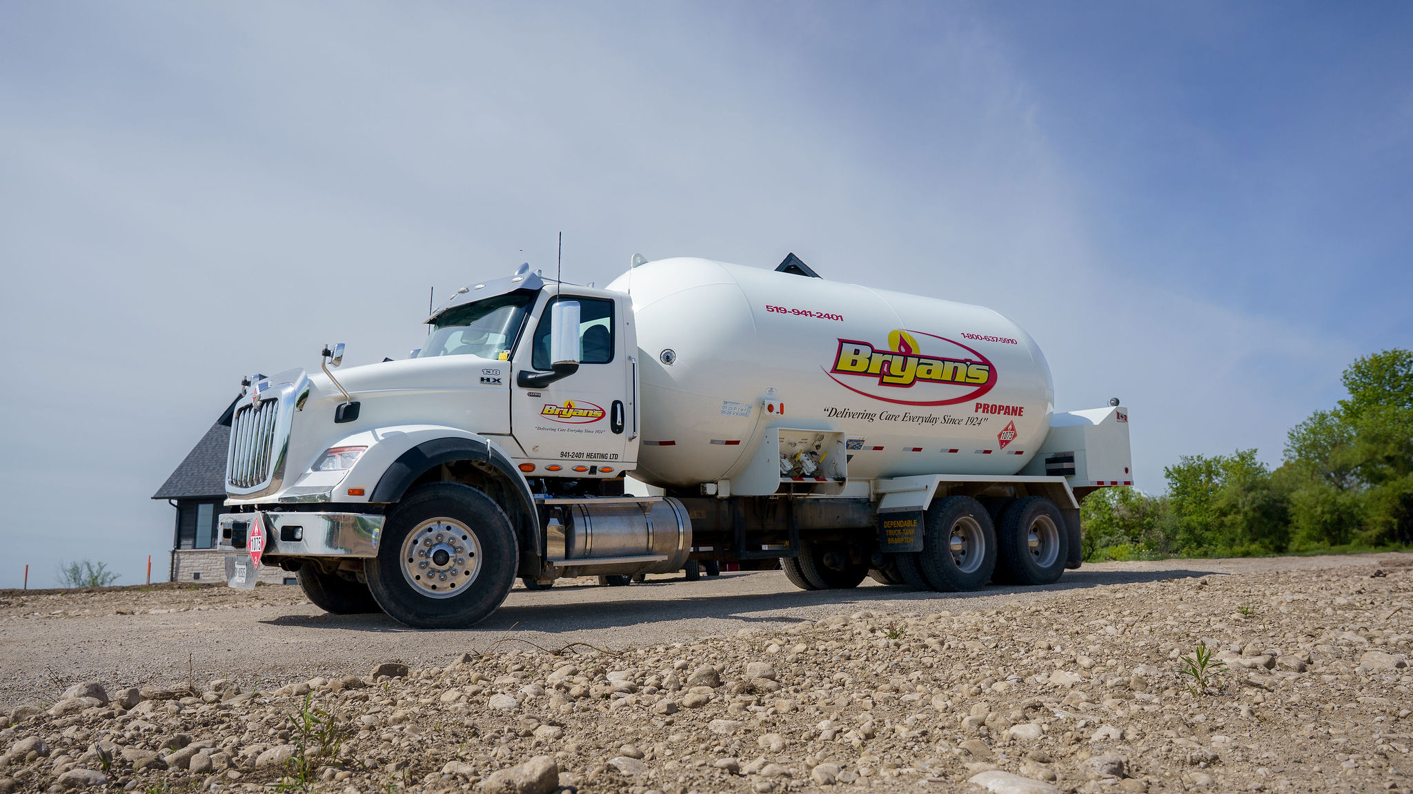 A large propane delivery truck parked on a gravel surface, with a logo on its side and a house in the background.