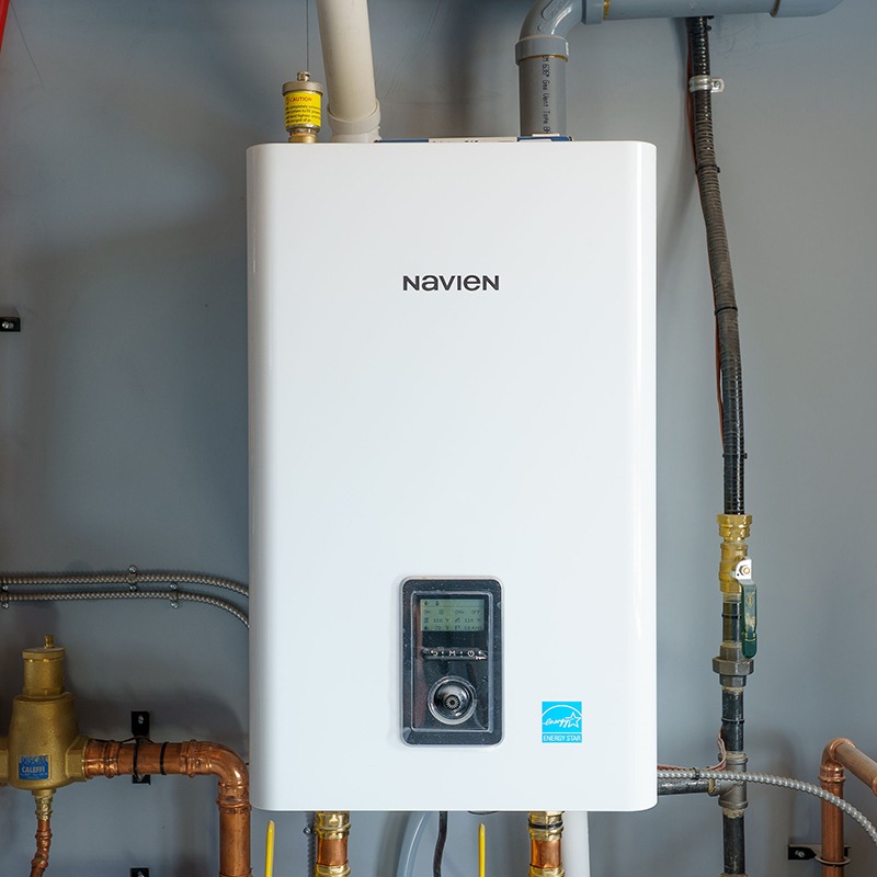 A Navien tankless water heater mounted on a wall with visible pipes and a digital control panel.