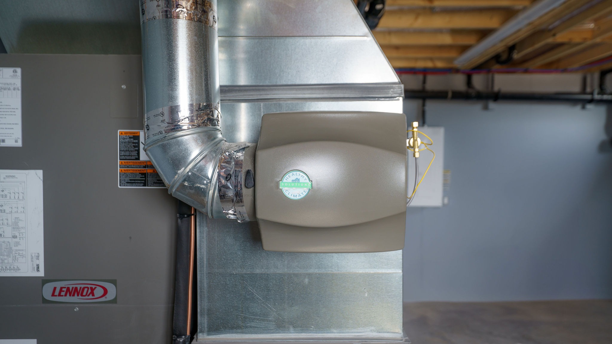 A basement scene featuring a Lennox HVAC system with ductwork and humidifier attached, against a gray wall and unfinished ceiling.