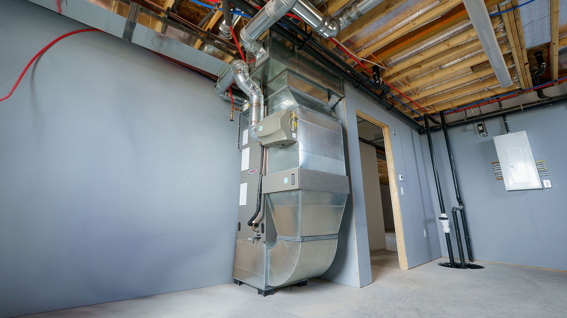 Basement room with exposed ducts and pipes, featuring a modern HVAC system. Concrete floor and unfinished ceiling with visible insulation.