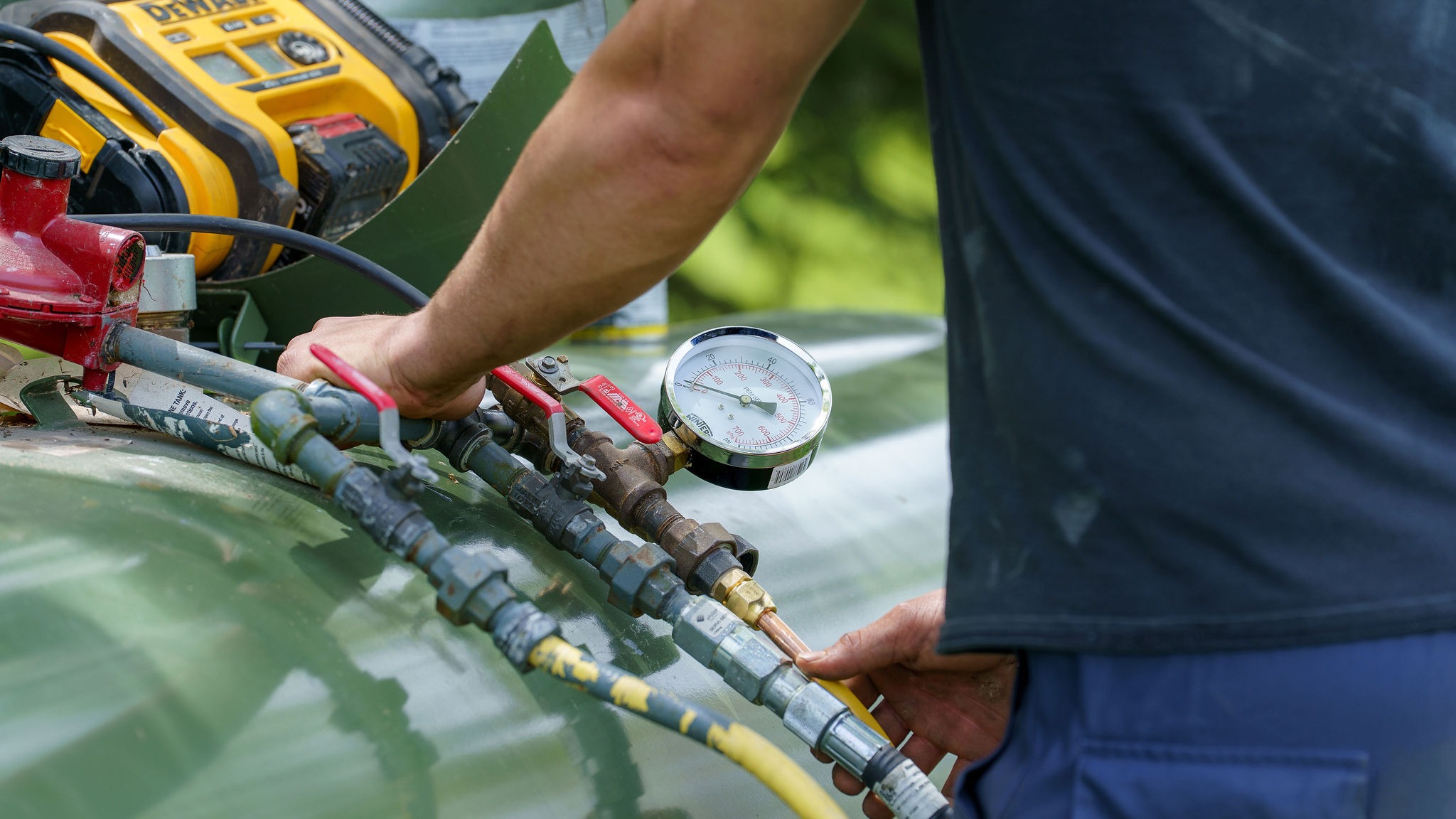 A person adjusts a gauge on industrial equipment, surrounded by pipes and valves, focused on precise measurement and maintenance tasks.