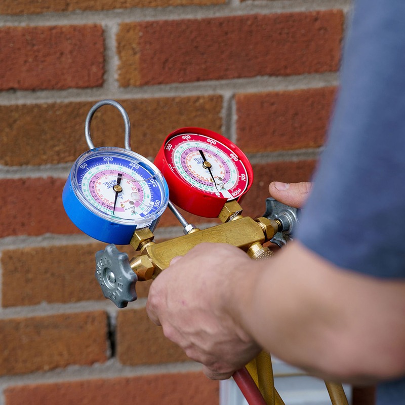A person adjusts red and blue pressure gauges against a brick wall, focusing on calibration or maintenance tasks.