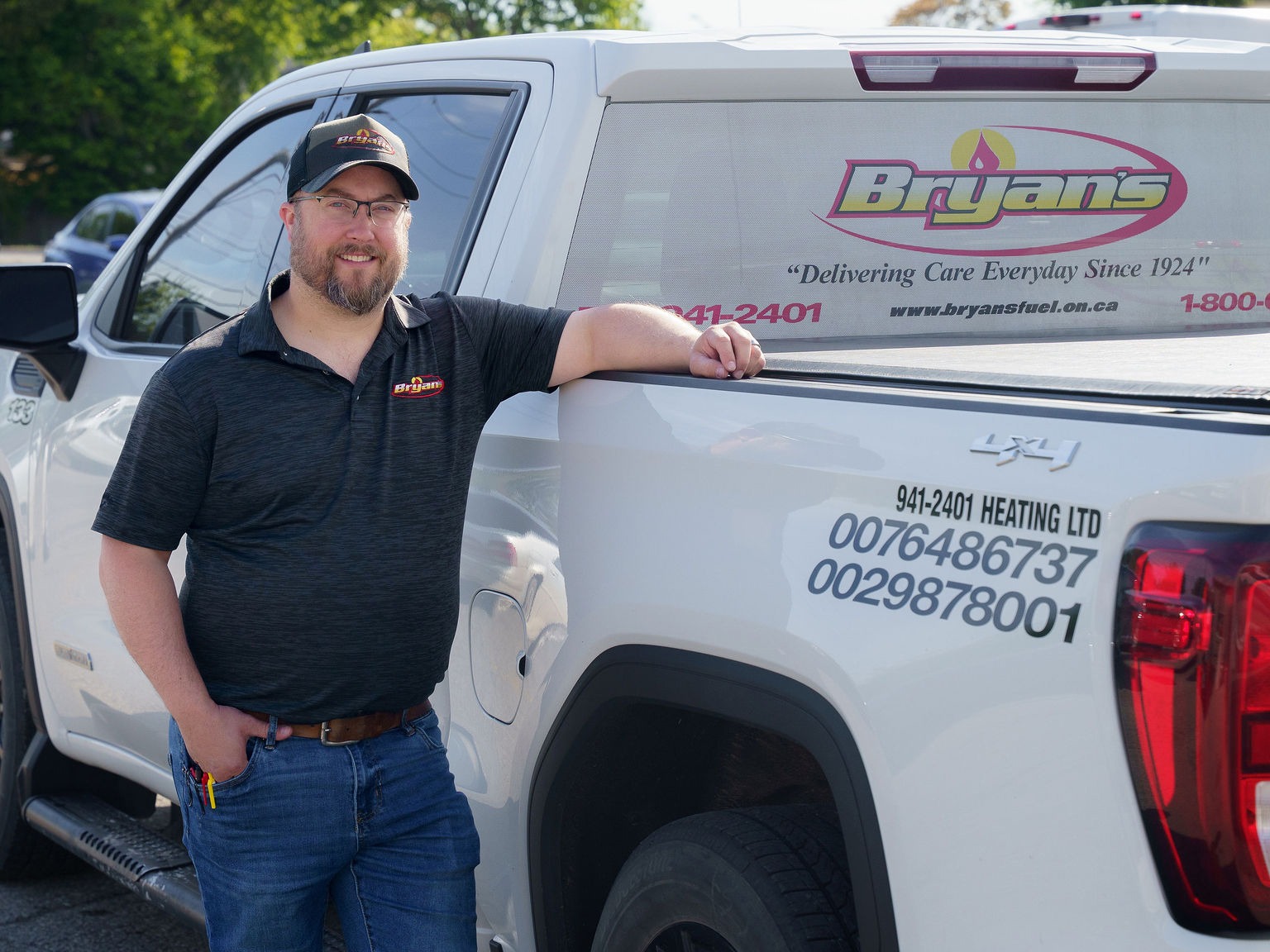 A person wearing a cap and branded shirt stands next to a truck with "Bryan's" signage in a parking area.