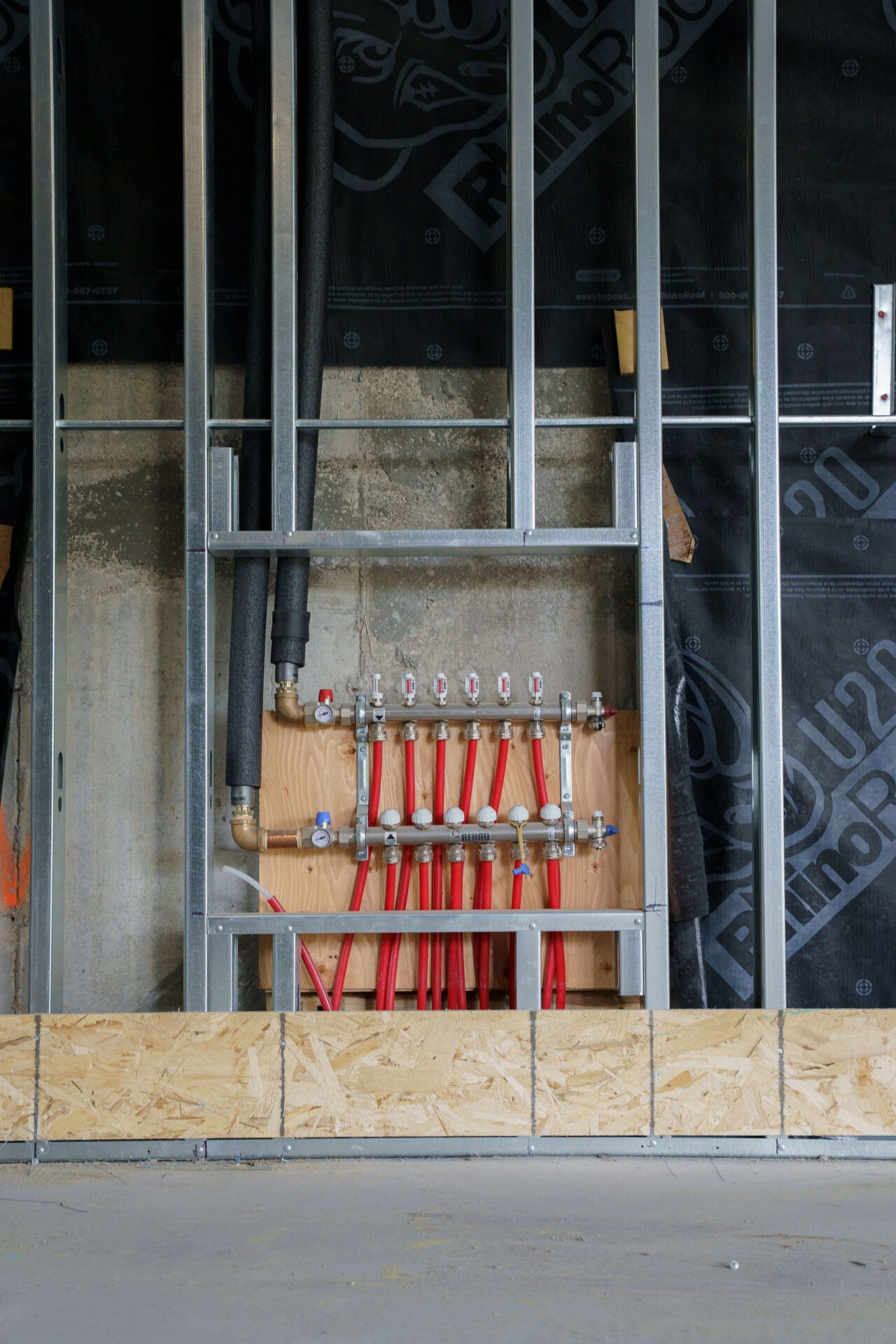 Construction site close-up showing exposed plumbing pipes and metal framing against a wooden and concrete wall, with no people present.