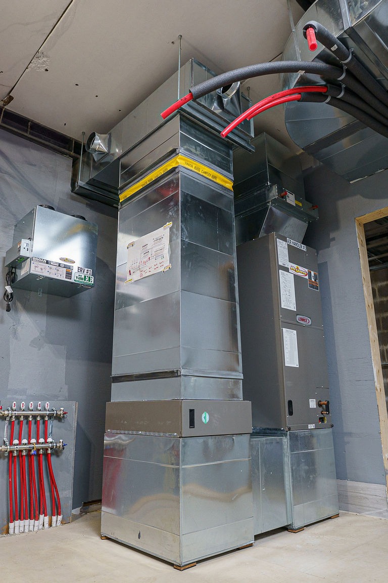 Industrial room with metal HVAC systems, ducts, and red piping against a gray wall. The setup appears organized and modern.