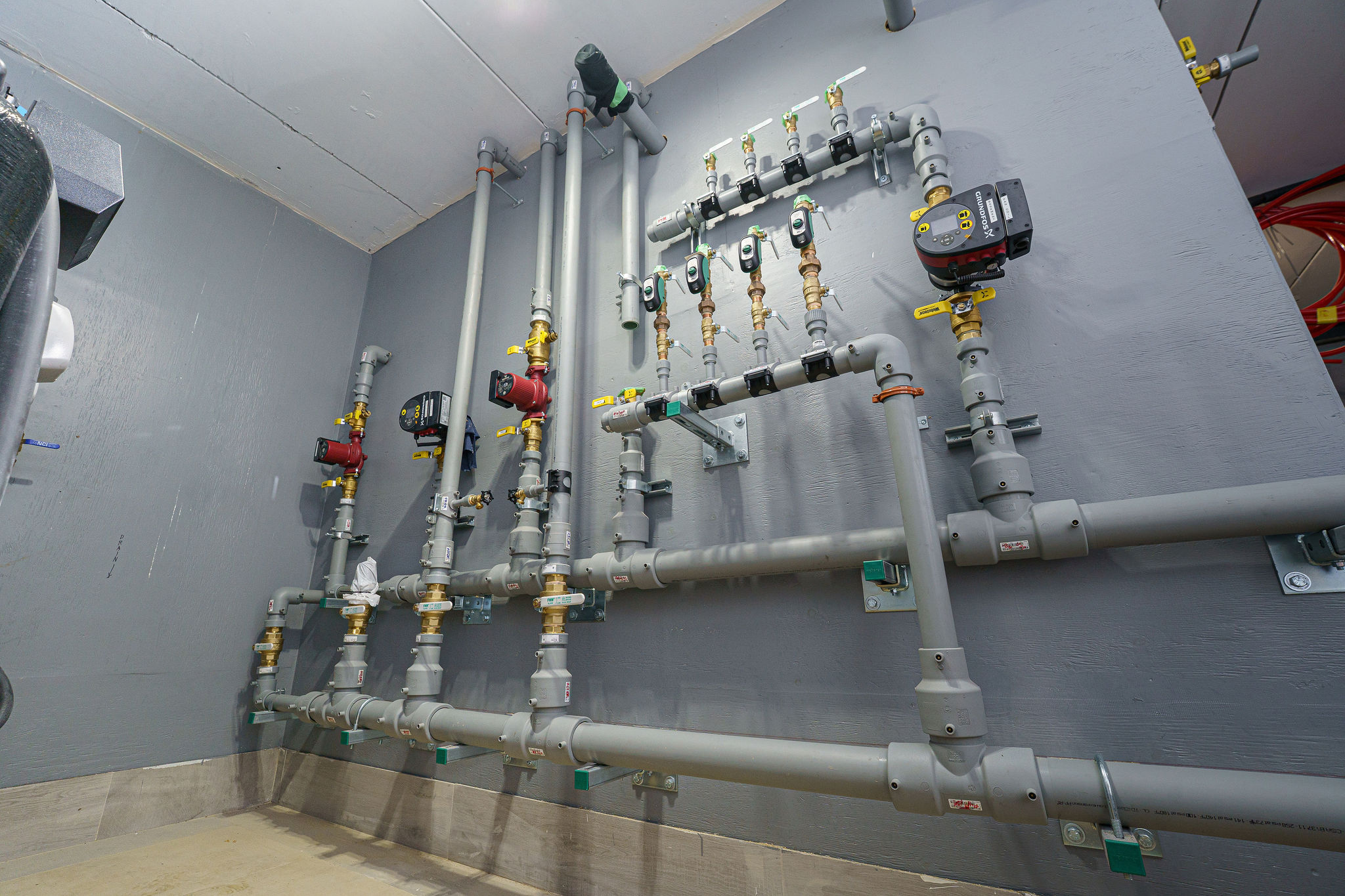 A technical room showcasing a network of industrial-grade plumbing pipes, valves, and gauges, mounted on a gray wall, with efficient organization.