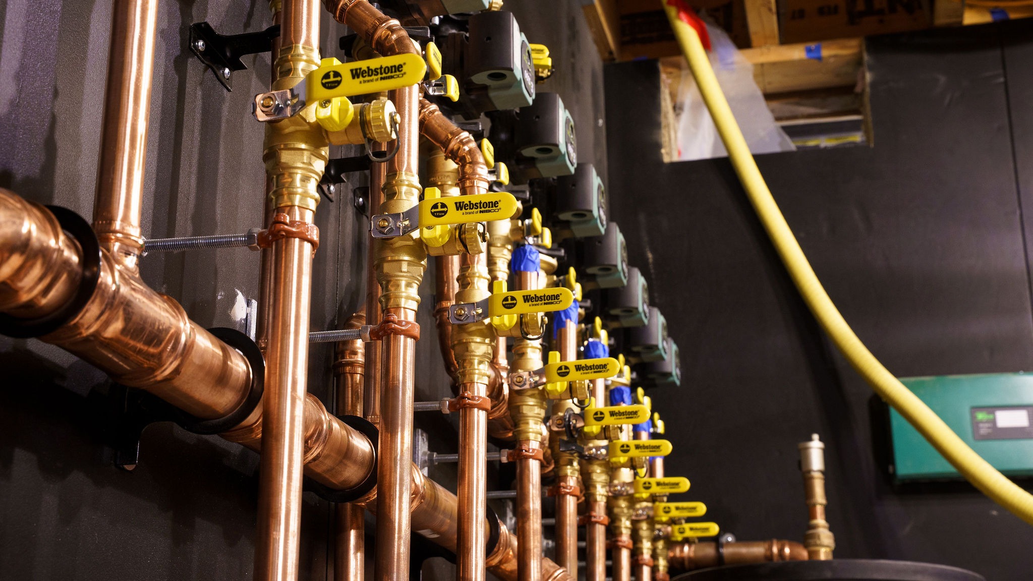 Copper plumbing valves and pipes with yellow Webstone handles are neatly arranged against a wall, showcasing an intricate system of water flow management.
