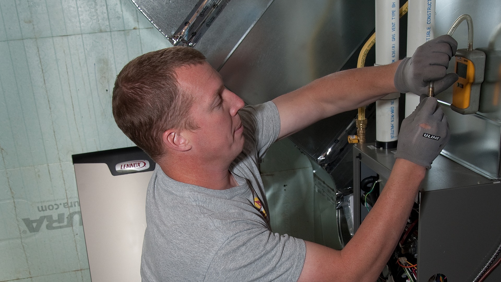 A person works on a HVAC system, wearing gloves and using a tool. The unit is branded with the Lennox logo.