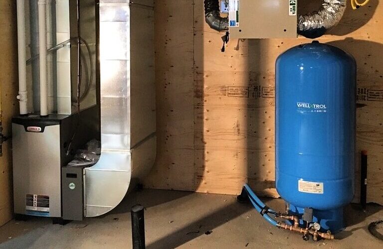 A basement utility room features a furnace and a large blue pressure tank marked "Well-X-Trol," with ductwork and pipes visible against a plywood wall.