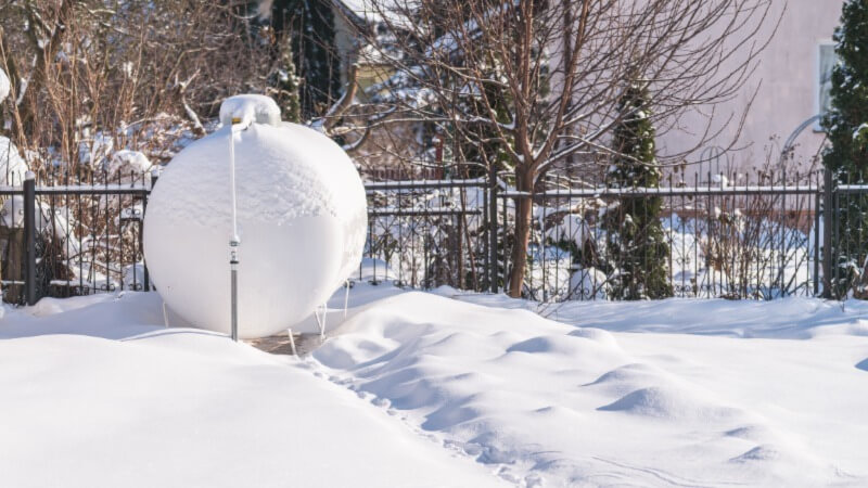 A photo of a residential propane tank in a yard in winter, covered in snow.
