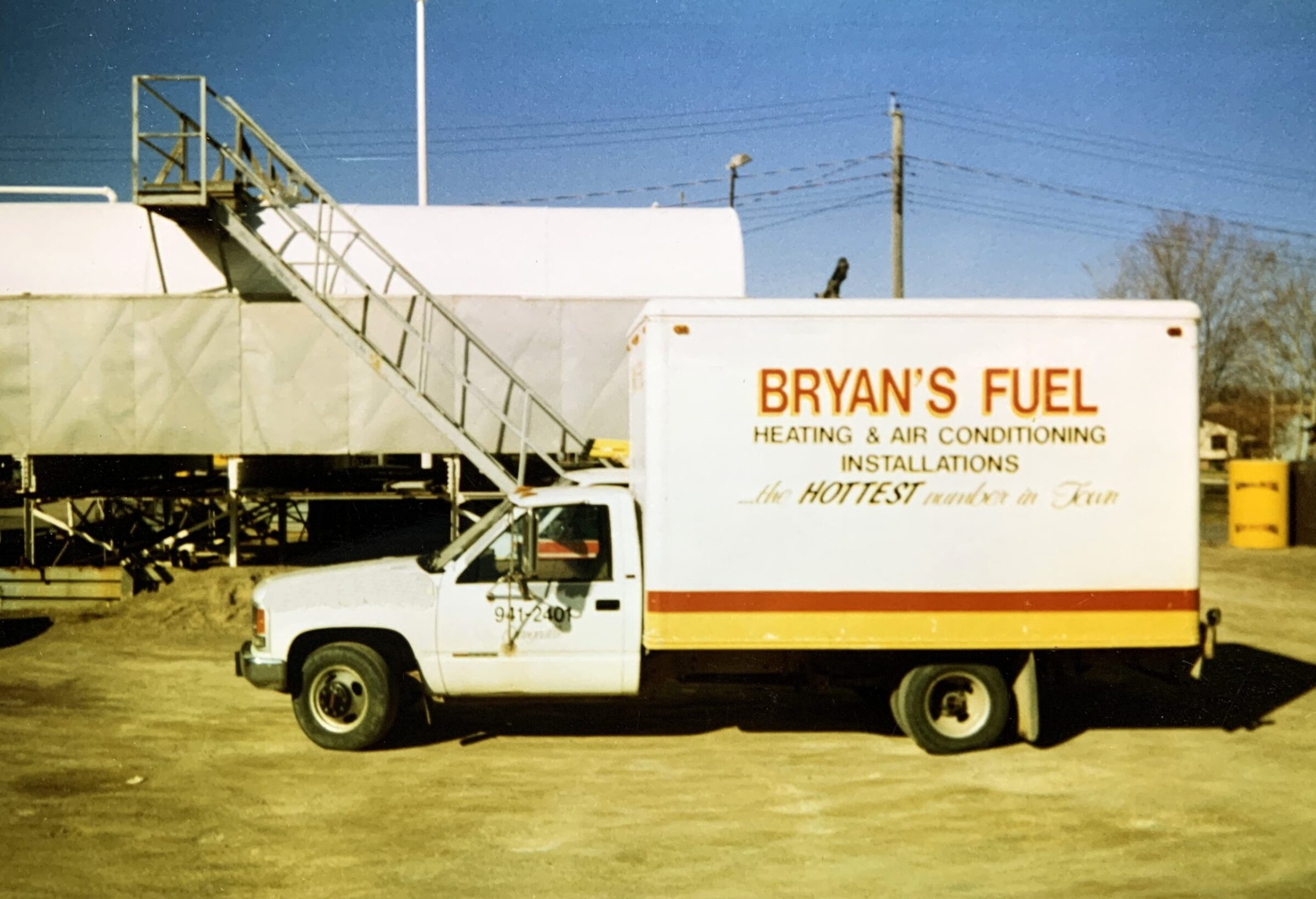 A truck with "Bryan's Fuel" branding is parked under a metal staircase on a sunny day, with sand and industrial equipment nearby.