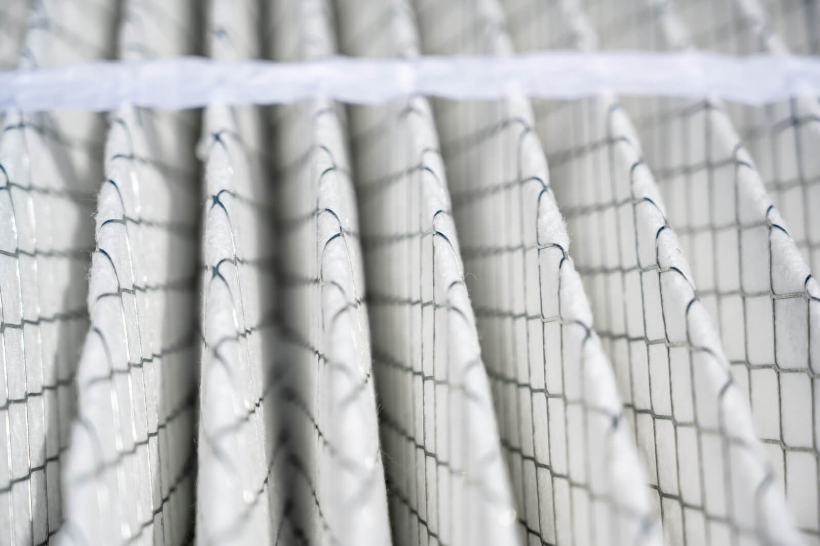 Close-up view of an air filter with pleated white material and grid pattern, showing detailed texture and structure under soft lighting.